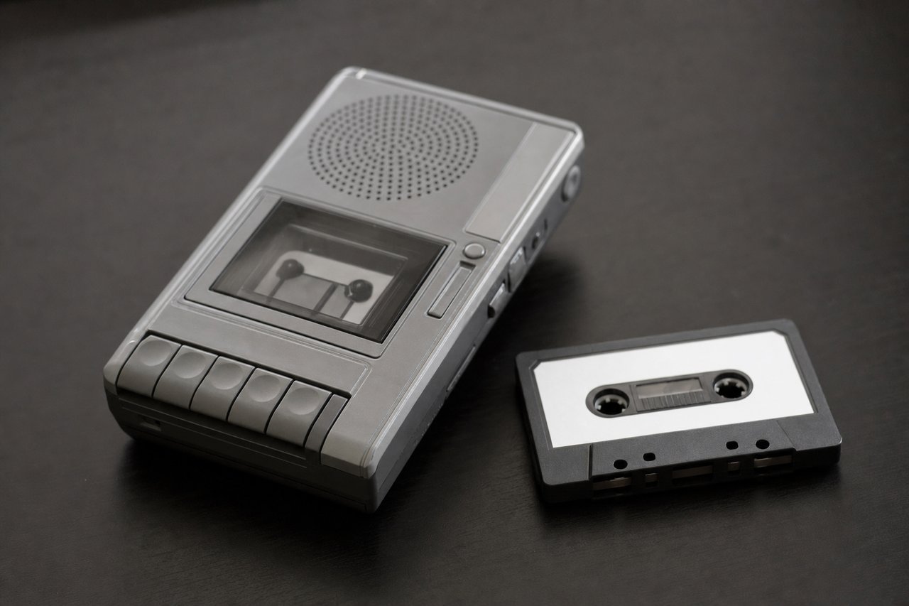 Ein Kassettendiktiergerät der 1990er neben einer unbeschrifteten Kassette