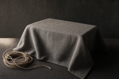 Ein rechteckiger Gegenstand unter einem grauen Tuch, daneben aufgerollte Schnur